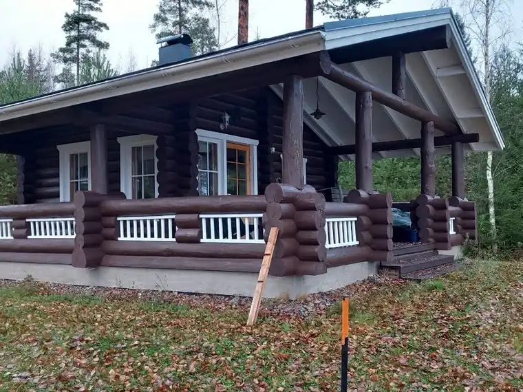 Tumedaks töödeldud ümarpalkmaja valge verandapiirdega