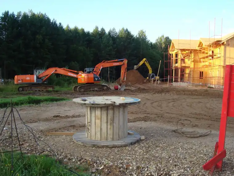 Ekskavaatorid platsil, taustal palkhoone